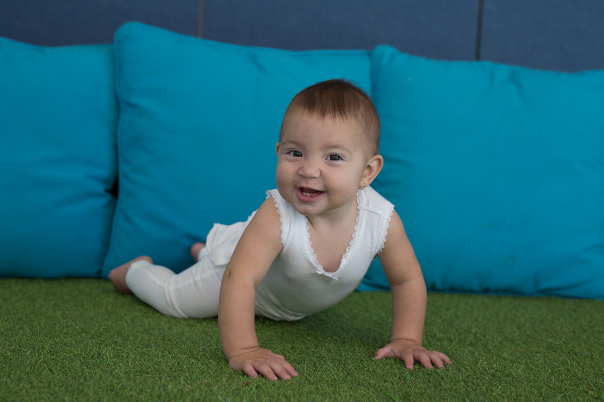 Baby with a big smile crawling on astroturf in front of blue cushions