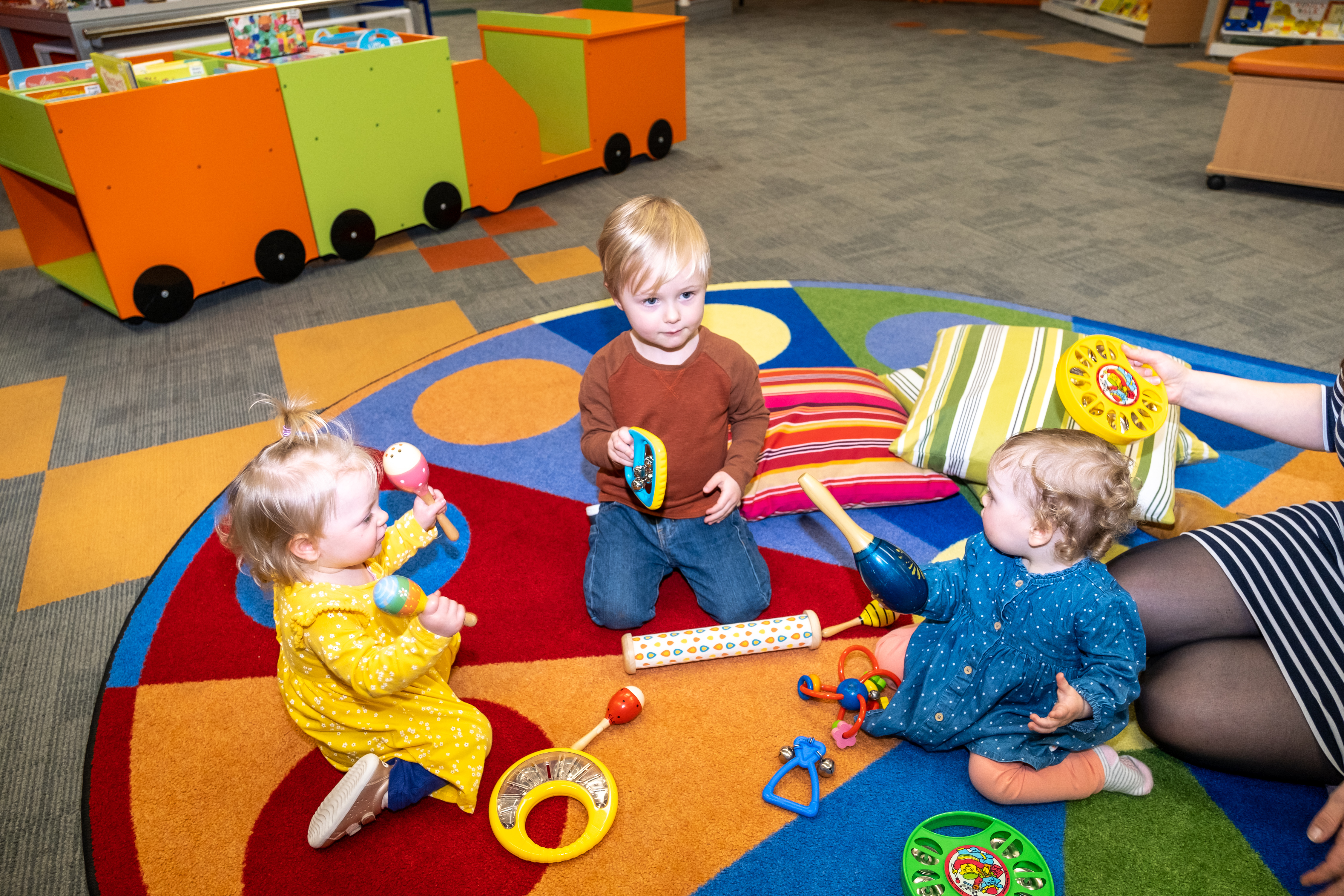 A brother plays musical instruments with his baby sisters who have musical rattles