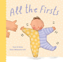 The book cover is a creamy yellow colour with the title “All the Firsts” in purple font. Below it, a child in a yellow and purple onesie takes their first wobbly steps while a pair of adult hands reach in from off the page, ready to steady them.